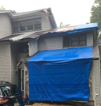 Damaged house roof covered with blue tarp during roof repair